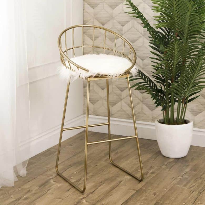 Gold bar stool with a white faux fur cushion next to a potted plant