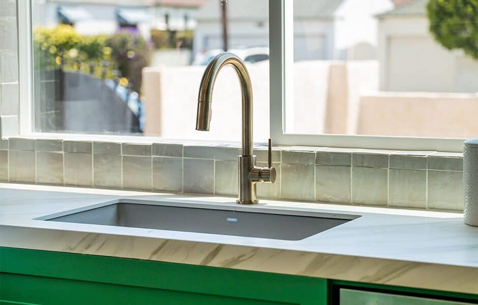 Kitchen sink with a gold faucet, green cabinets, and tiled backsplash