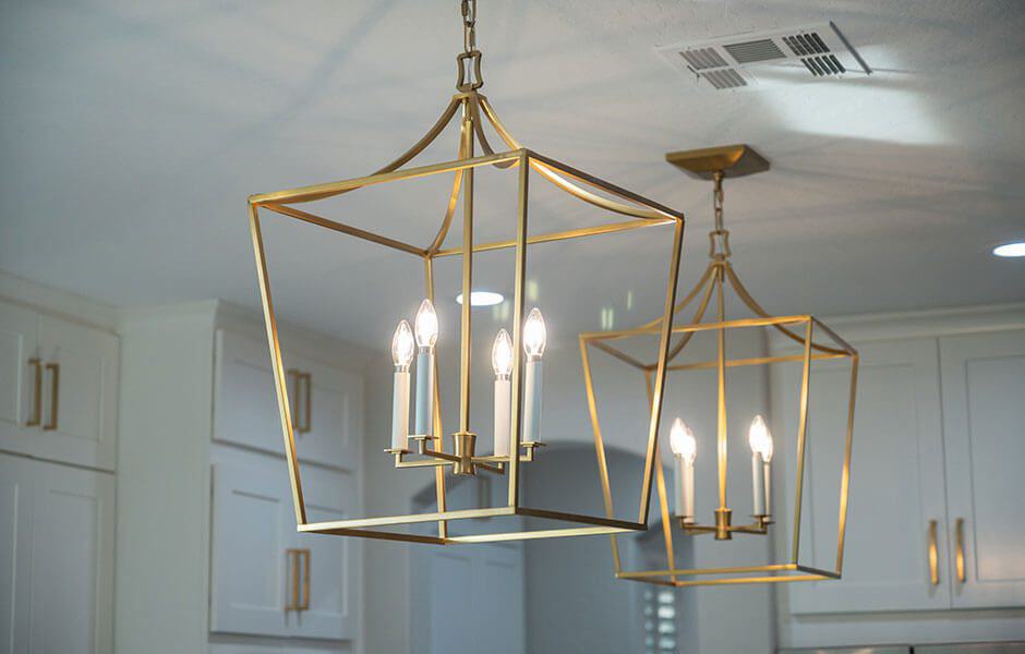 Two gold geometric pendant chandeliers with candle-style bulbs hanging in a kitchen