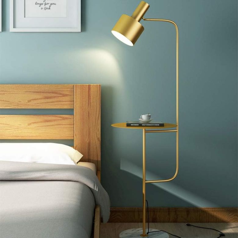 Gold floor lamp with built-in side table next to a wooden bed and blue wall
