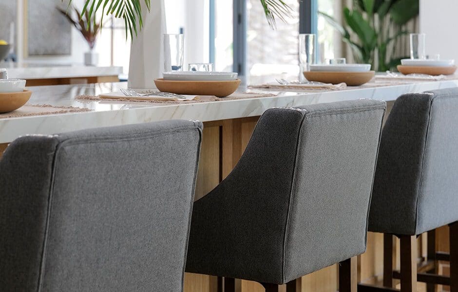 Modern kitchen island with gray upholstered bar stools and place settings with bowls and glasses