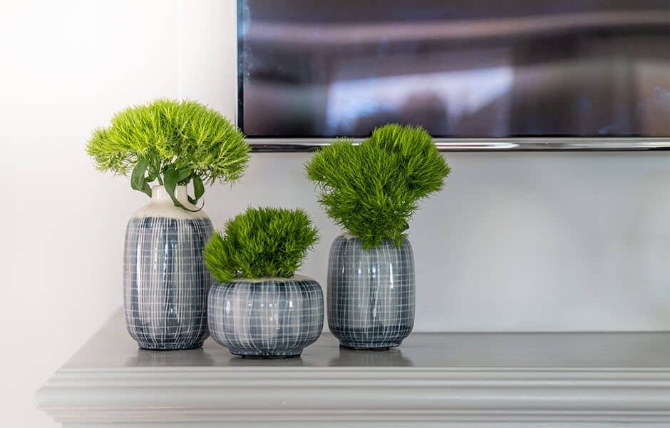 Trio of modern ceramic vases with vibrant green foliage displayed on a mantel