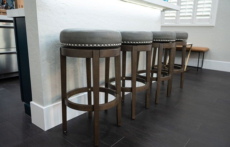 Row of wooden barstools with cushioned seats and nailhead trim in a modern kitchen