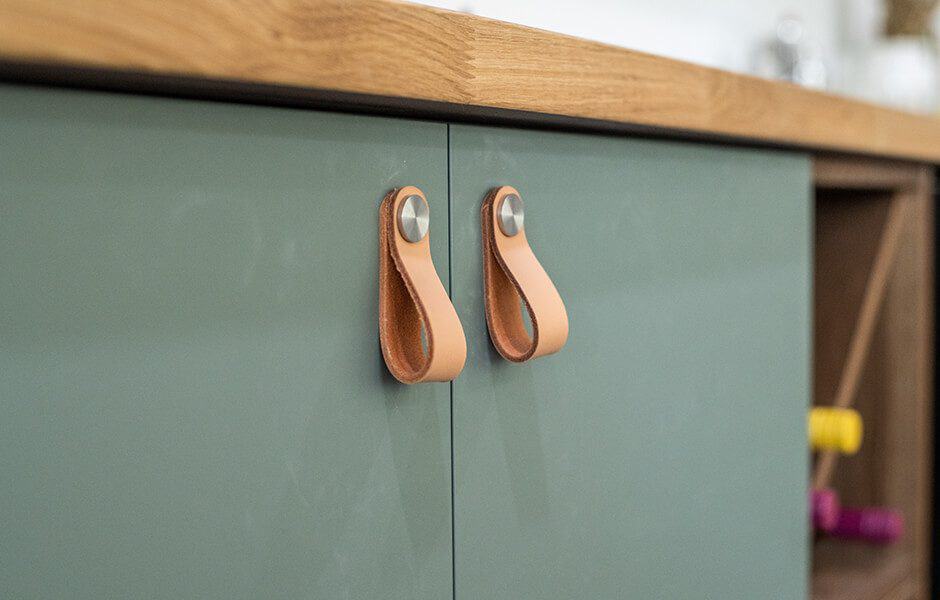 Green cabinet with leather loop handles and a wooden countertop