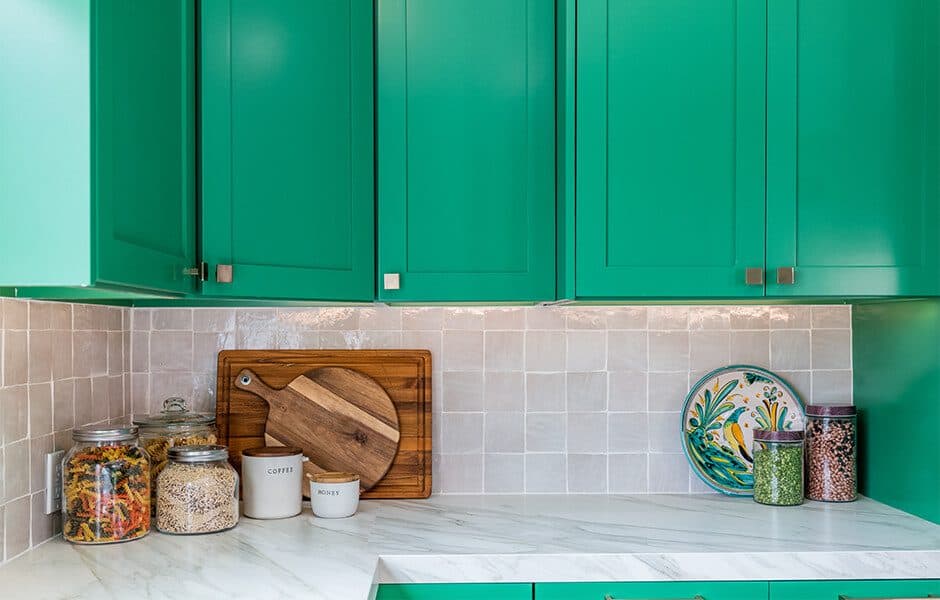 Vibrant kitchen with green cabinets, tiled backsplash, and organized countertop