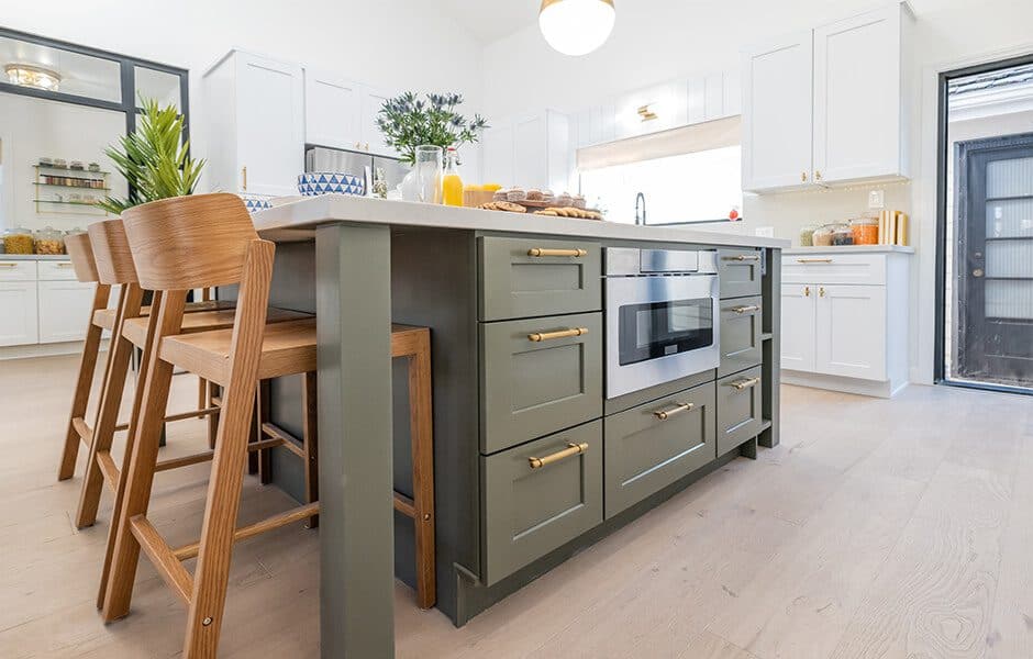 Kitchen with a green island, gold hardware, built-in microwave, and wooden bar stools