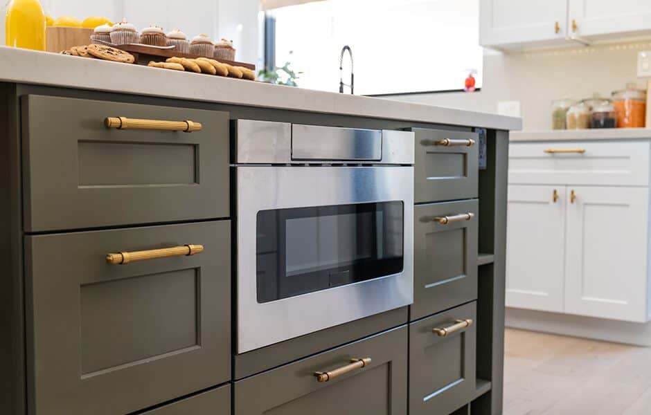Close-up of a kitchen island with green cabinets, a microwave, and baked goods on the counter