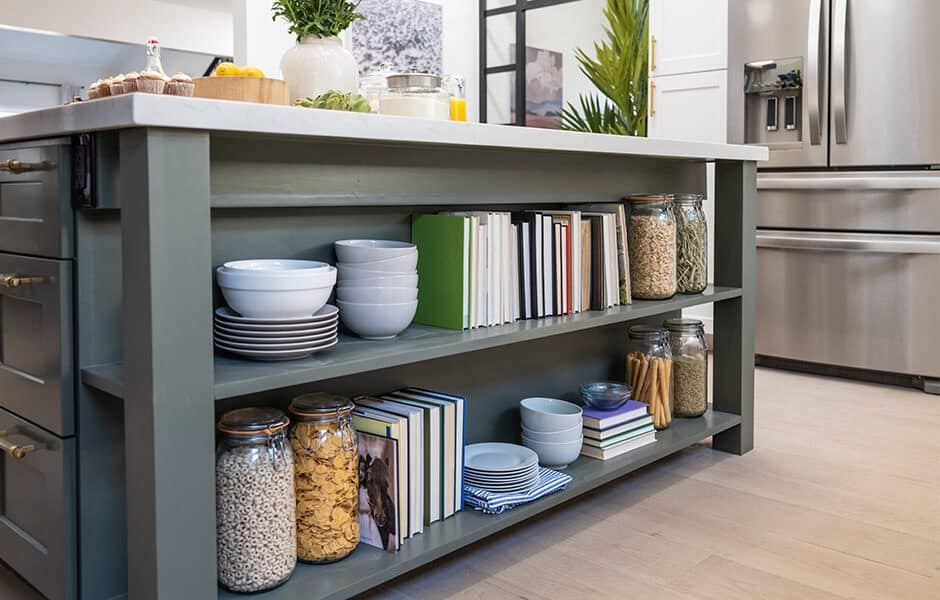 Organized kitchen island with bowls, plates, jars of cereal and pasta, and books neatly arranged on open shelves