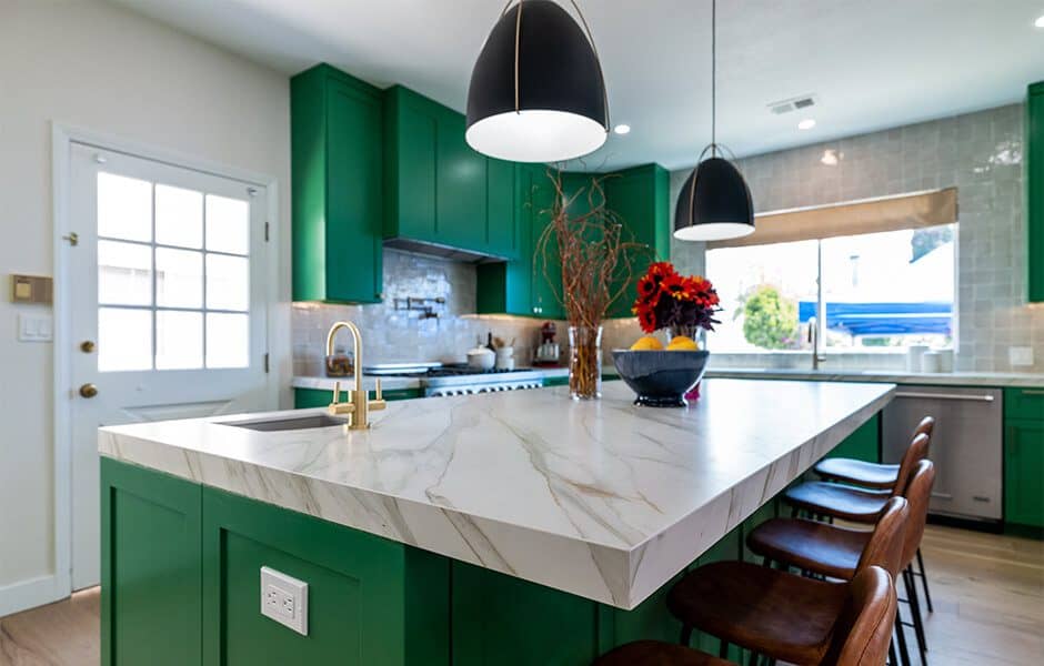 Bright kitchen with green cabinets, a large marble countertop island, pendant lighting, and wooden barstools