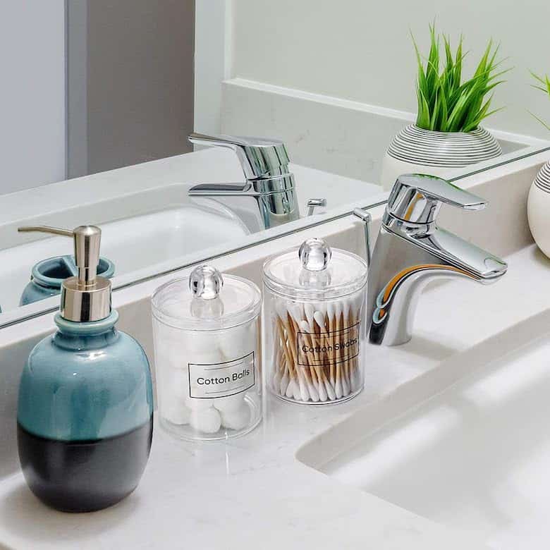 Bathroom sink with a soap dispenser, jars of cotton balls and swabs, and small potted plants