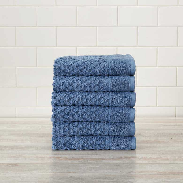 Stack of folded blue textured towels on a wooden surface with a white tiled background