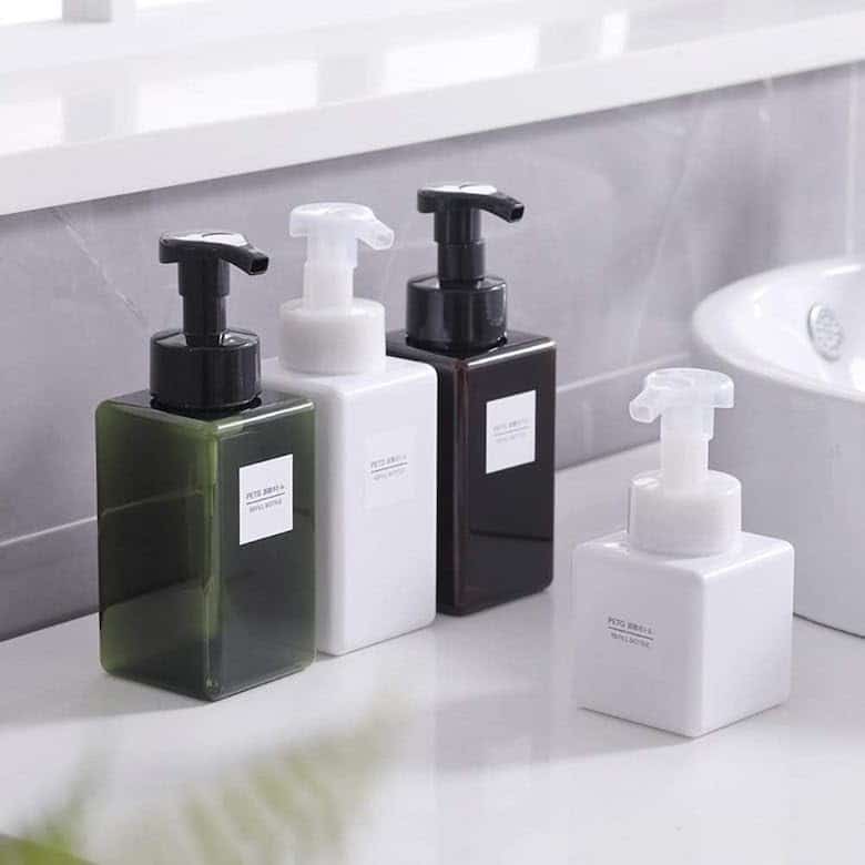 Set of square pump bottles in green, white, and black on a bathroom counter
