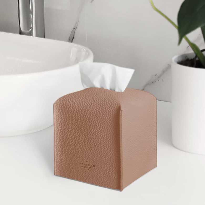 Brown textured tissue box cover on a white bathroom counter beside a sink and plant