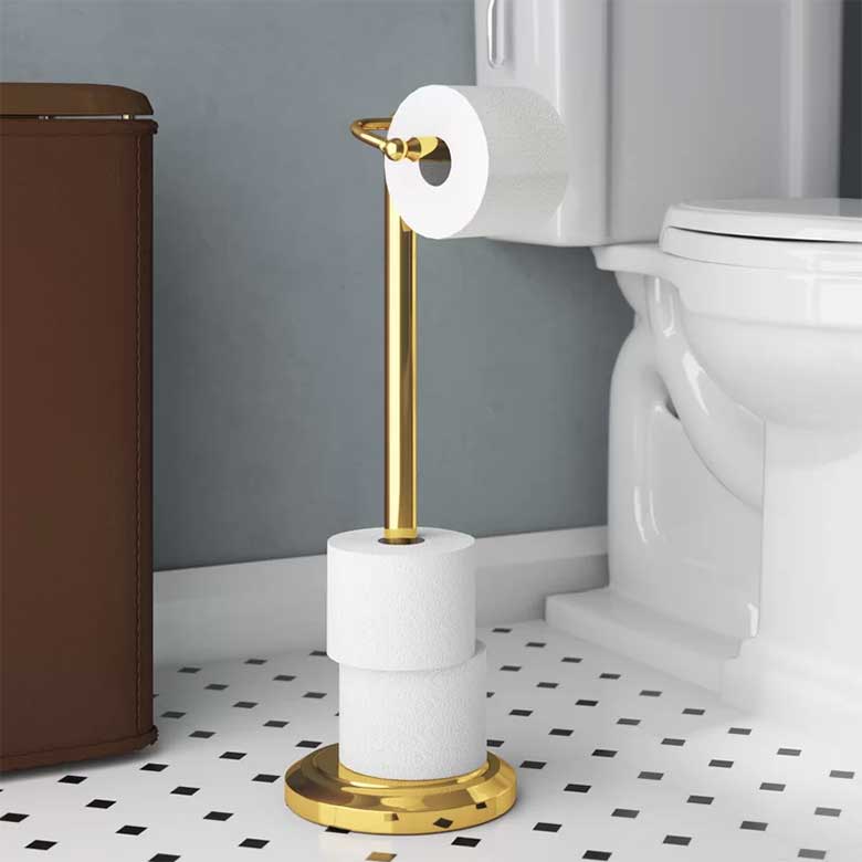 Gold toilet paper holder stand with extra rolls stacked at the base in a bathroom