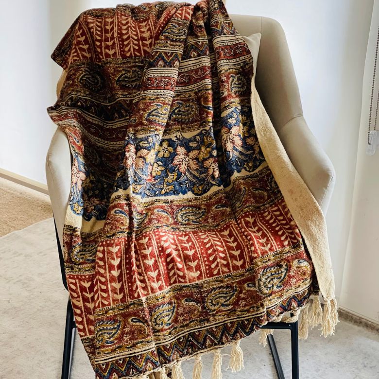 Ornate patterned throw with rich red, blue, and gold hues draped over a beige accent chair