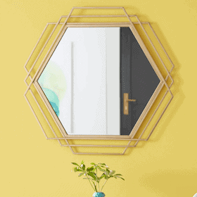 Hexagonal mirror with layered gold frame on a bright yellow wall above a small vase with green foliage