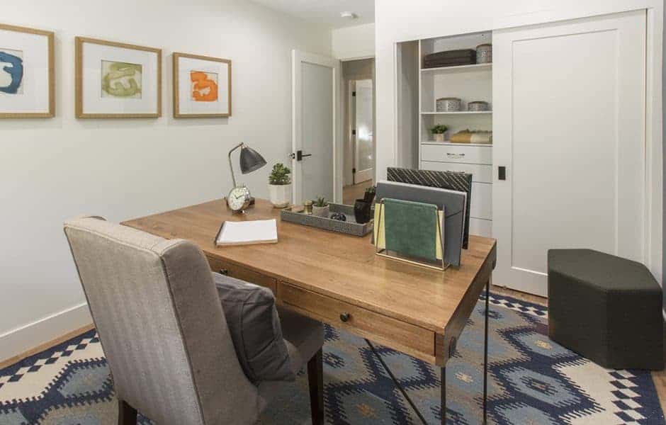 Home office with wooden desk, upholstered chair, wall art, and built-in shelving