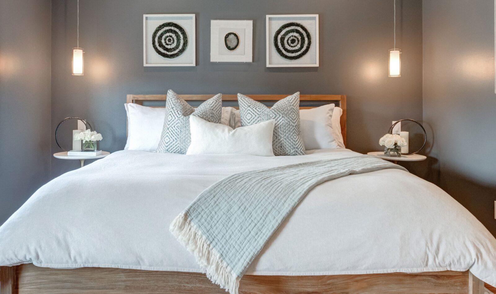 Cozy bedroom with a neutral bed setup, gray accent wall, geometric pillows, and pendant lights
