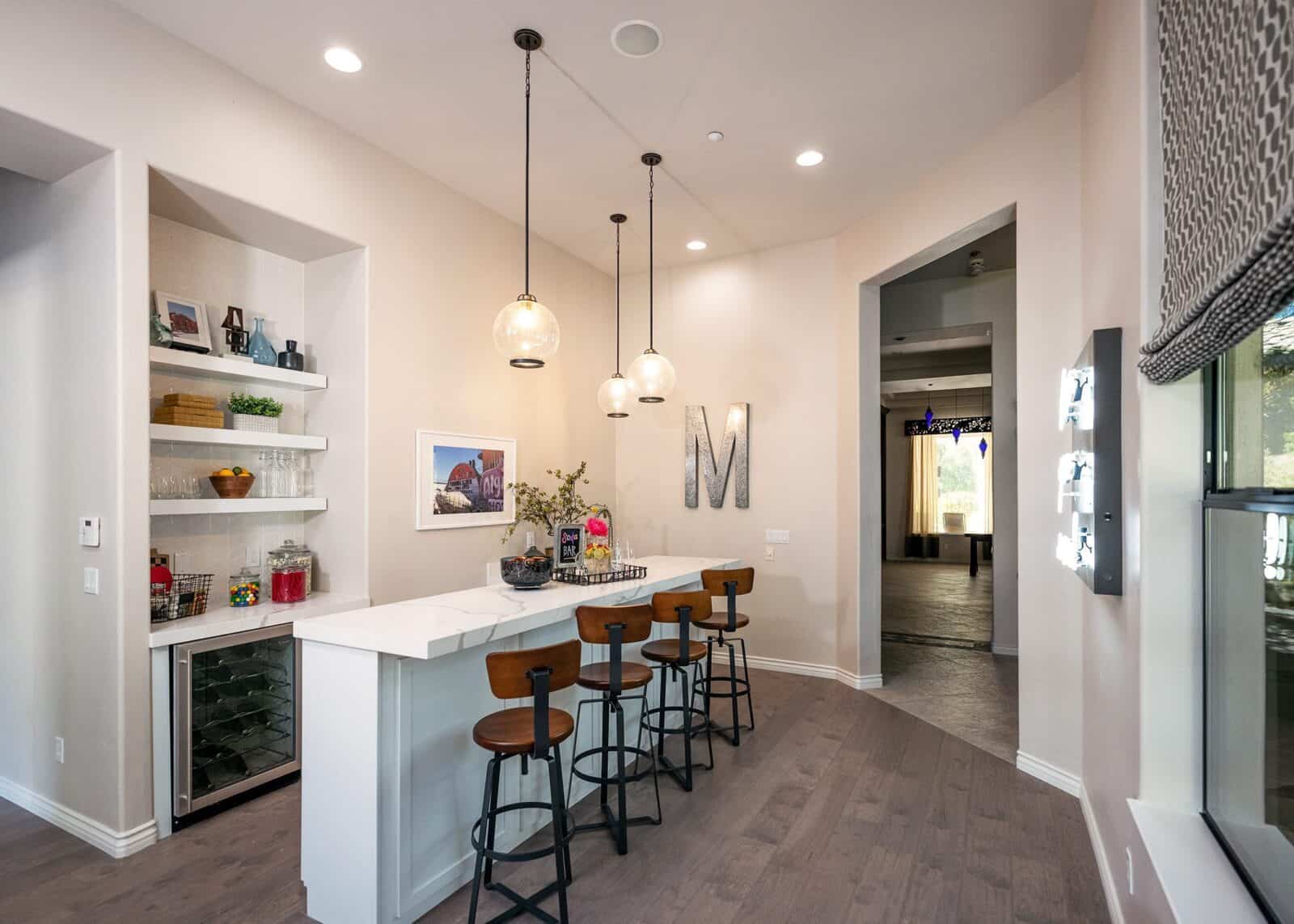 Kitchen bar with white countertop, wooden stools, pendant lights, and a wine cooler