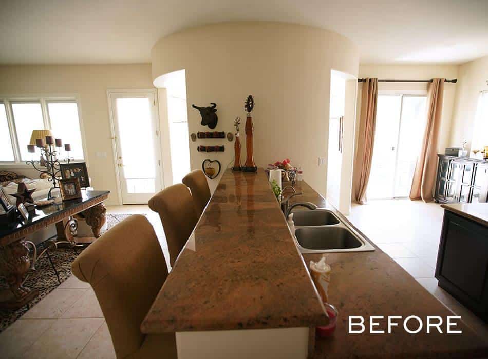 A before image of a Kitchen with a long granite countertop, double sink, and open layout leading to a living area