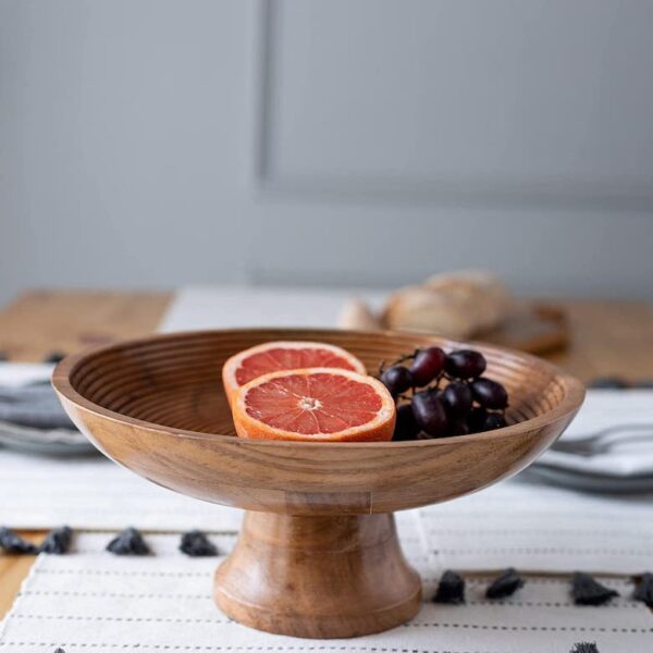 Wooden pedestal fruit bowl with sliced grapefruit and grapes on a dining table