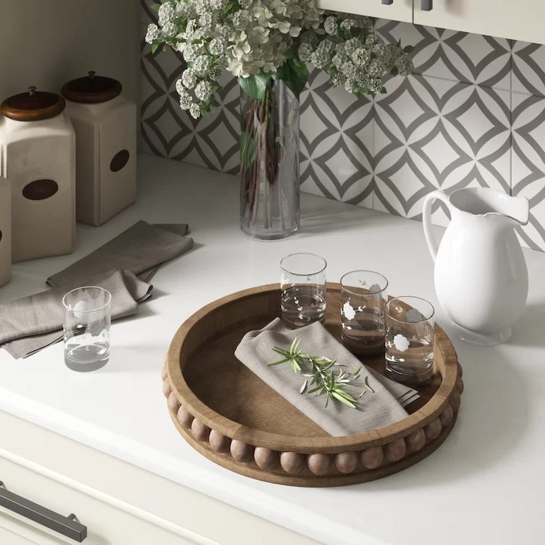Decorative kitchen counter with wooden tray, glasses, napkins, and floral arrangement