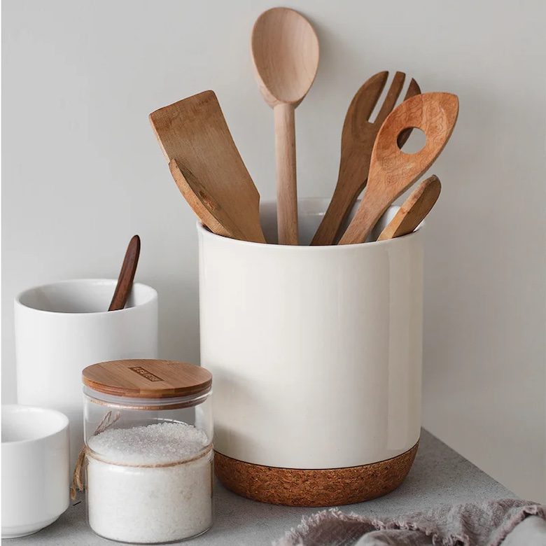Ceramic container holding wooden kitchen utensils beside cups and a jar of sugar