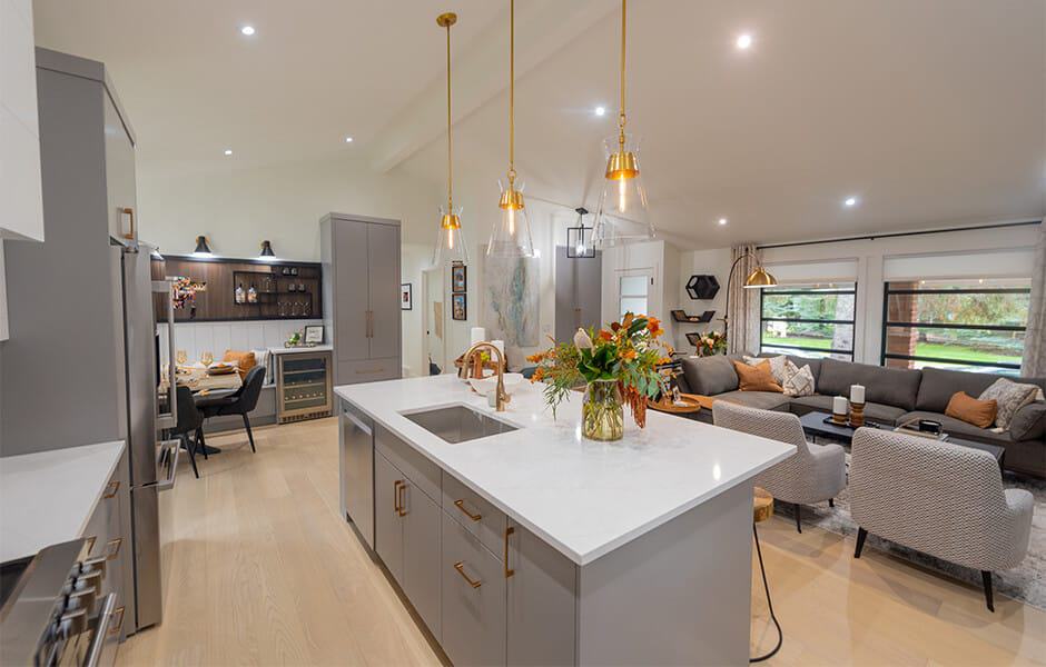 Open-plan kitchen and living room with a large white quartz island, gray cabinets, and gold pendant lights
