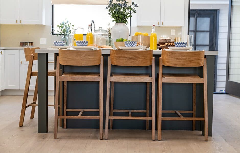 Modern kitchen with a large island, wooden barstools, and a breakfast setup with juice and fruit