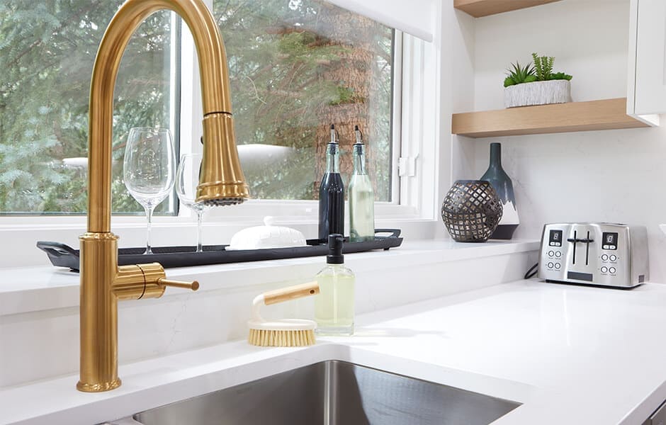 Clean and functional kitchen countertop with a gold faucet, white quartz, and a wooden shelf