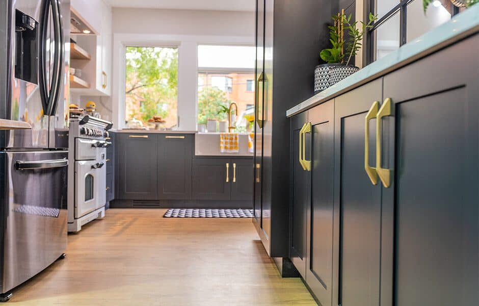 Modern kitchen with dark cabinets, gold handles, stainless steel appliances, and large windows