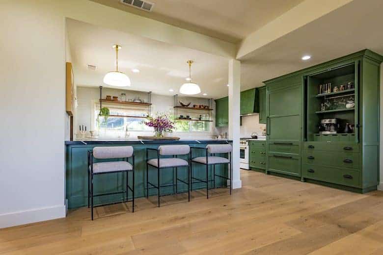 Kitchen with green cabinets, island seating, pendant lights, and open shelving