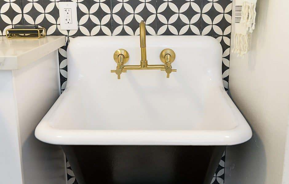 Stylish utility sink with a white basin, gold faucet, and black-and-white geometric tile backsplash