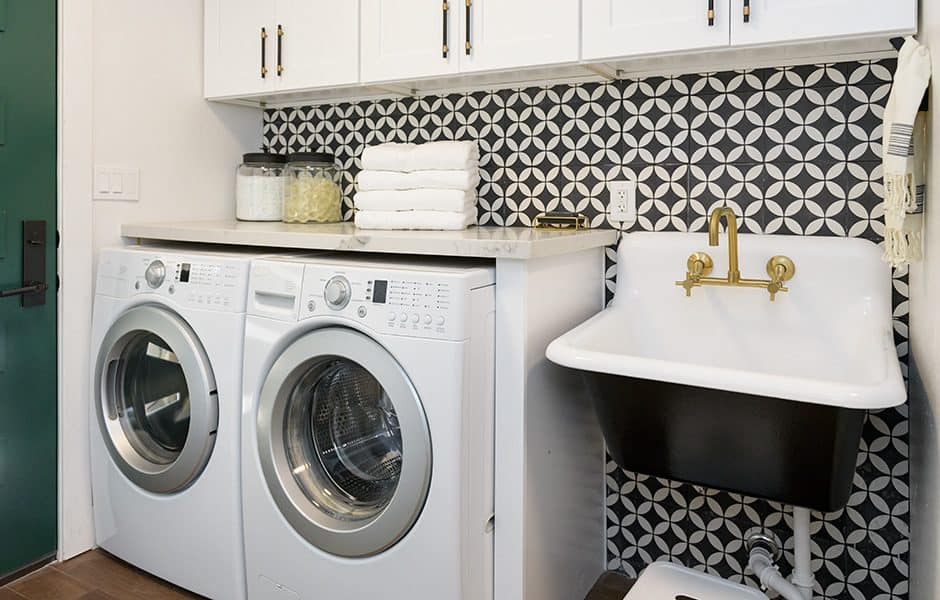 Laundry room with stacked washer and dryer, black sink, and brass faucet