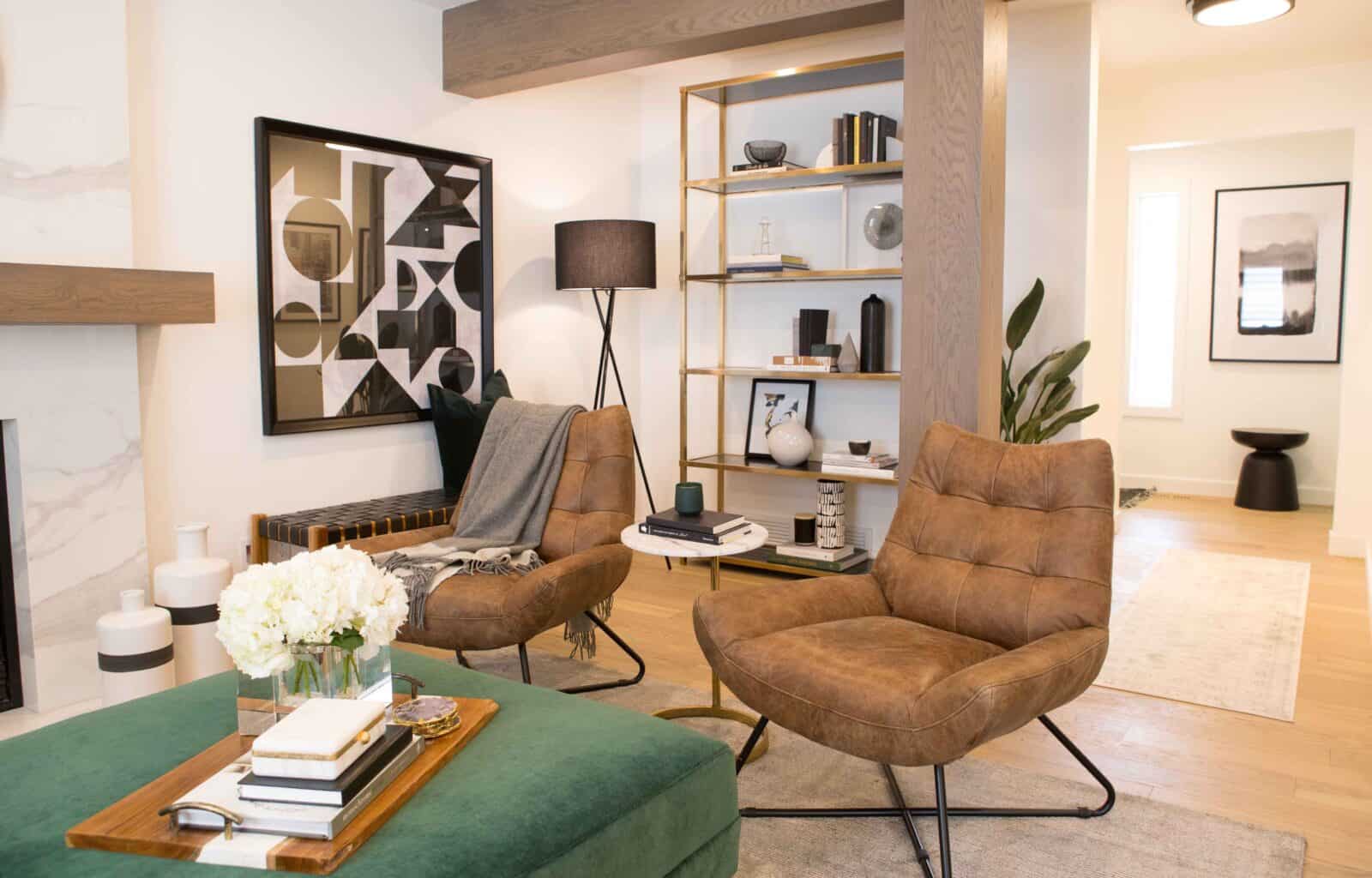 Living room with brown leather chairs, a green ottoman, a gold shelving unit, and modern decor