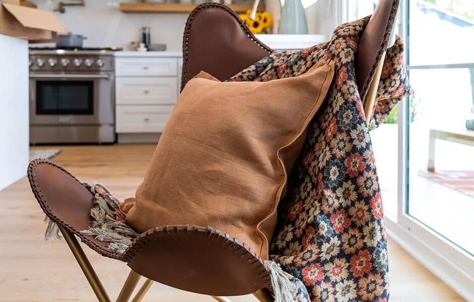 Cozy leather chair with a burnt orange pillow and patterned throw blanket in a modern kitchen setting