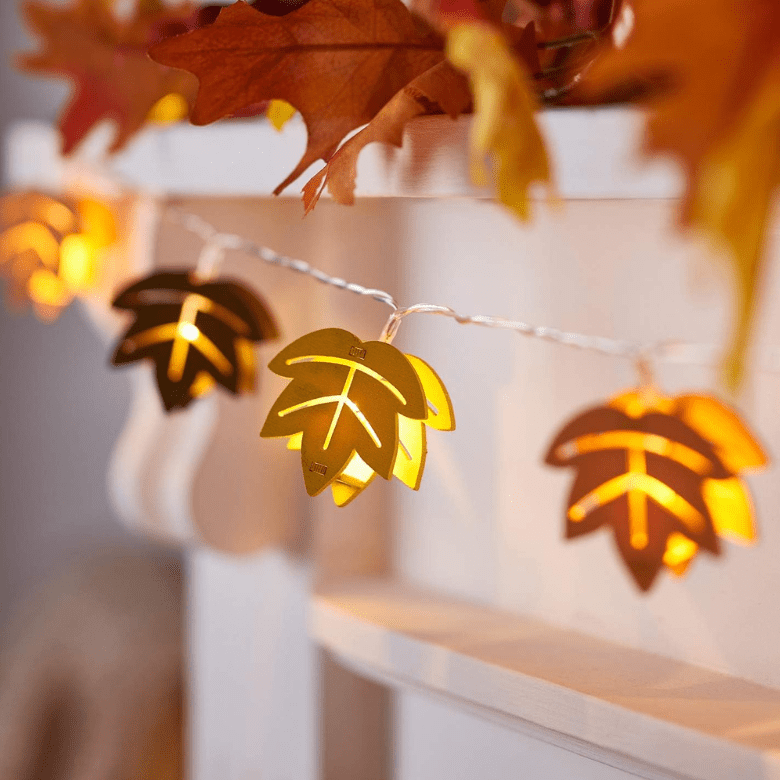 Fall leaf string lights glowing along a mantel decorated with autumn foliage