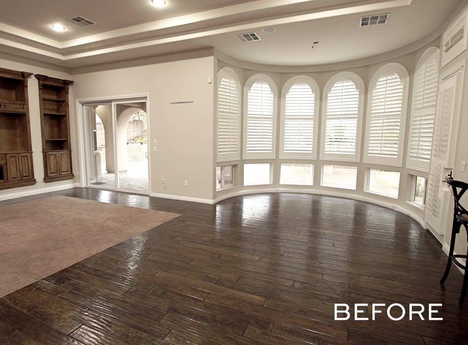 Spacious living room with dark wood flooring, built-in shelves, and large arched windows with white shutters
