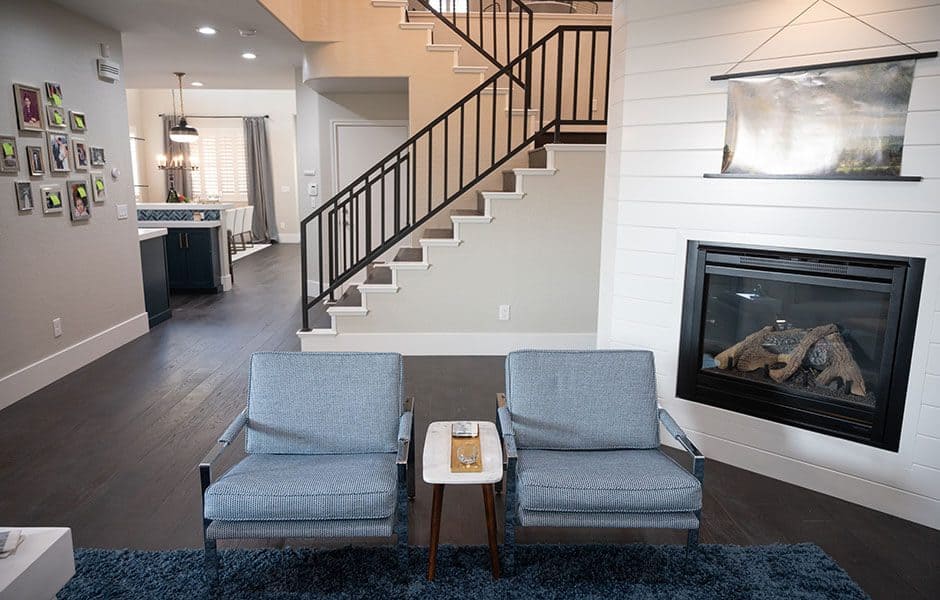 Modern living room with white shiplap wall, fireplace, armchairs, and staircase
