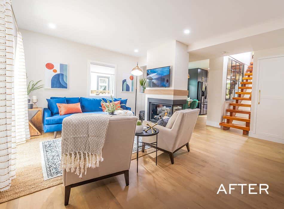 Bright living room with a blue sofa, accent chairs, fireplace, and staircase