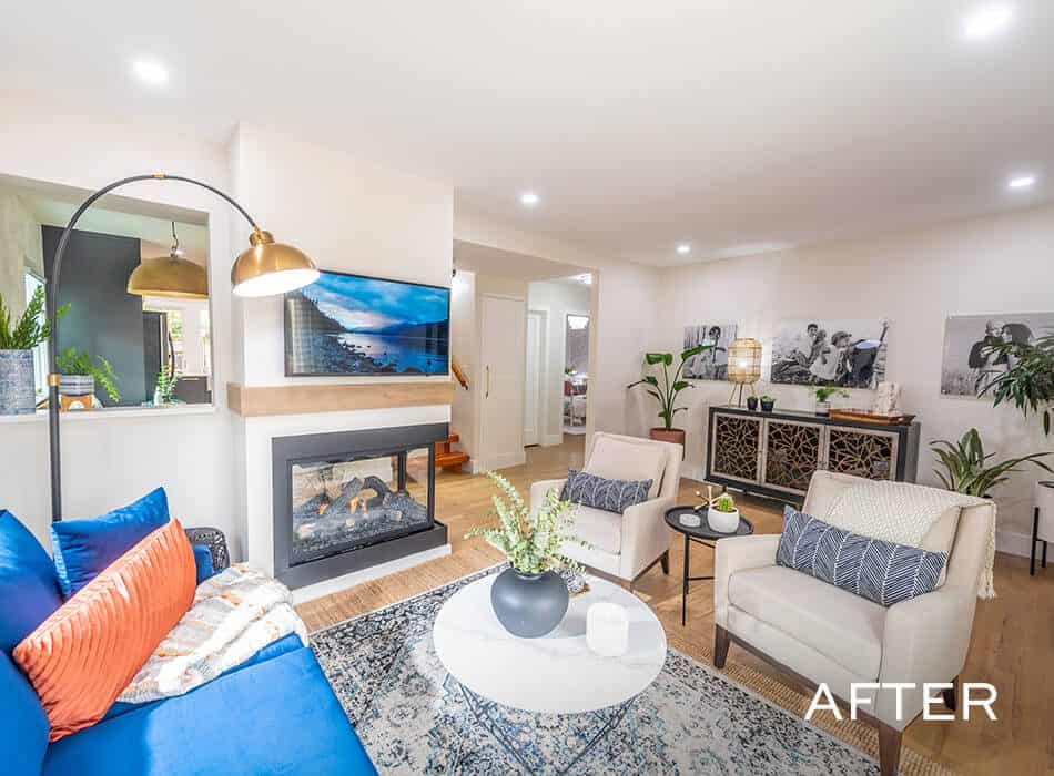 Bright living room with a fireplace, blue sofa, white armchairs, and decorative accents