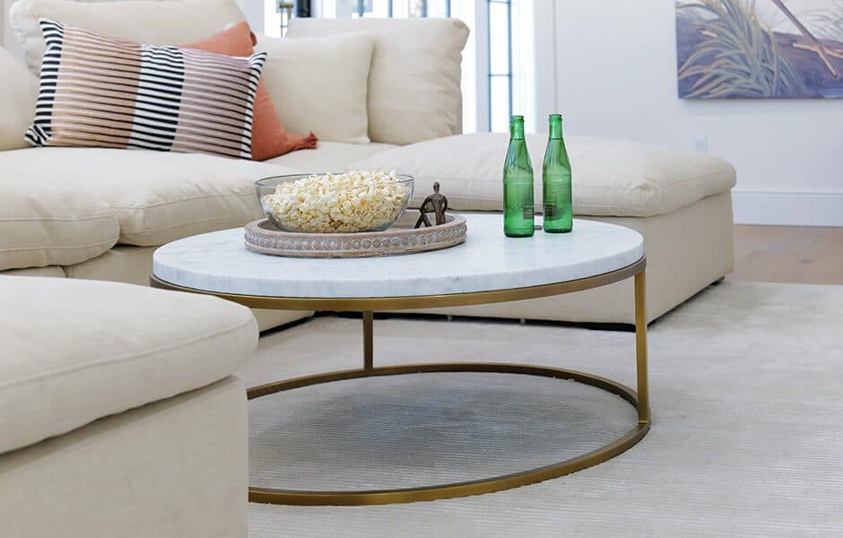Round marble coffee table with gold frame in front of a beige sectional sofa