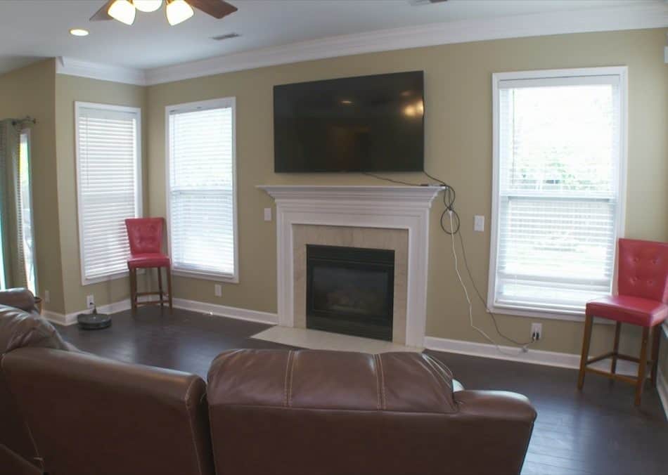 Living room with a fireplace, mounted TV, leather seating, and two red chairs by the windows