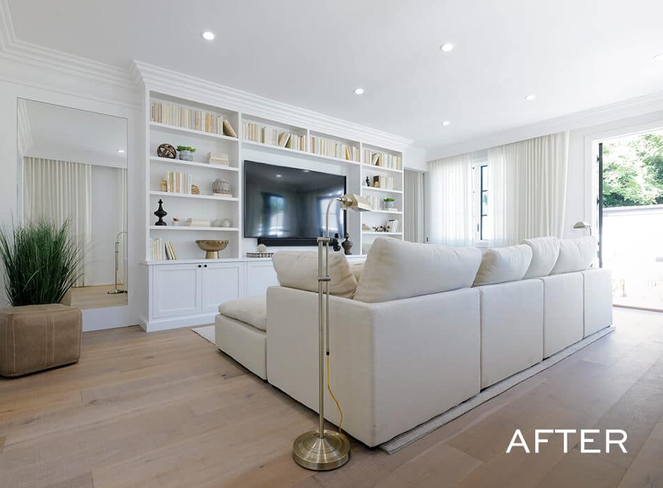 Modern living room with a white sectional sofa, built-in shelving, a large TV, and natural light from floor-to-ceiling windows