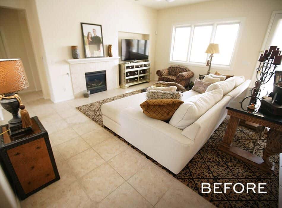 Dated living room with beige walls, a white fireplace, and a patterned rug (before renovation)