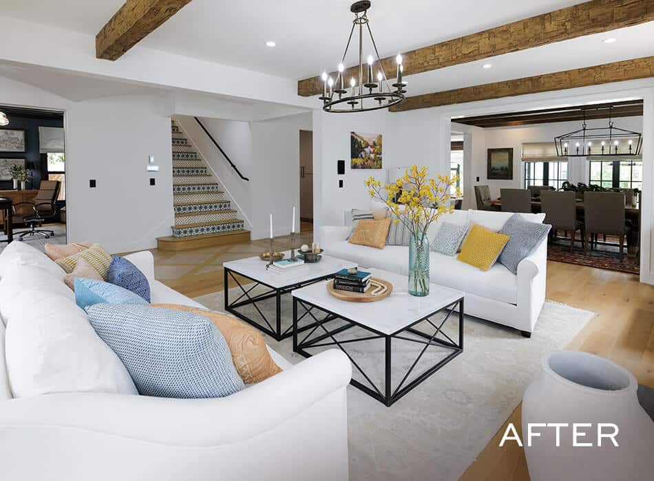 Modern living room with white sofas, colorful pillows, and wood beams.