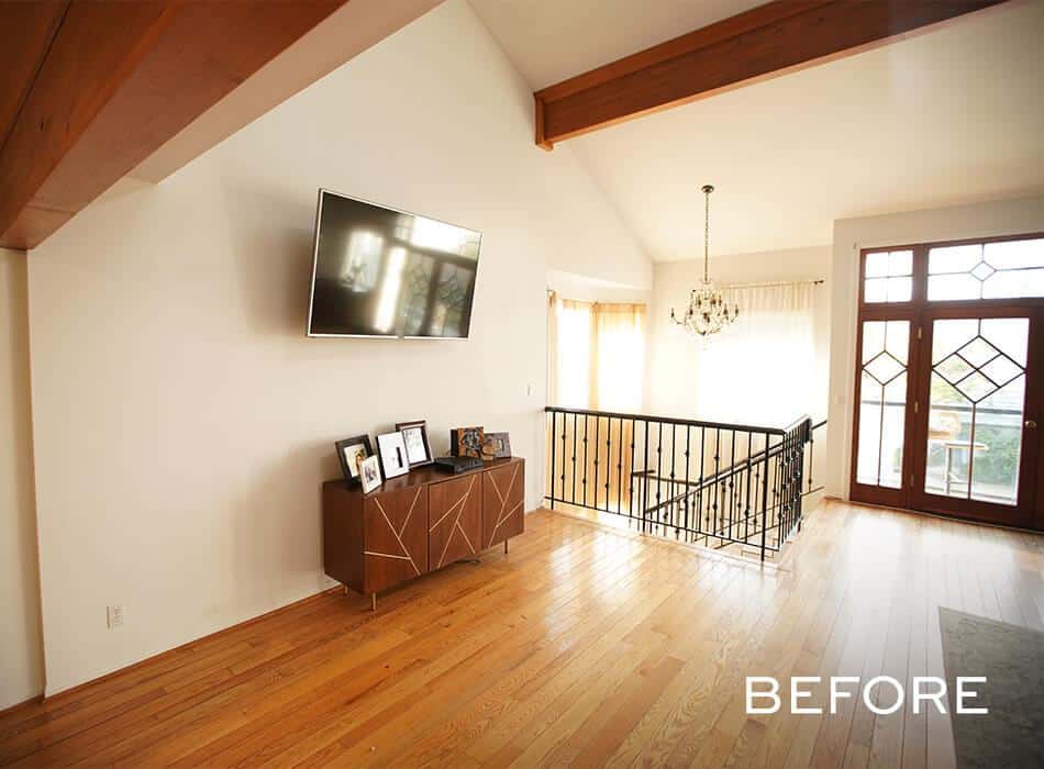 Before image of spacious living room with vaulted ceilings, TV, console table, and staircase