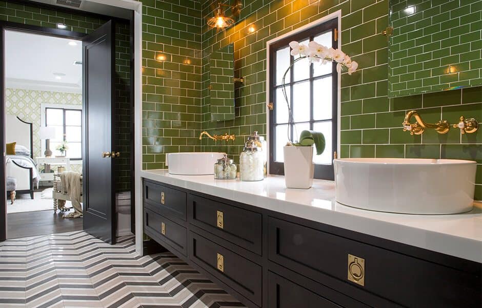 Elegant bathroom with green tiles, black vanity, gold fixtures, and a herringbone floor