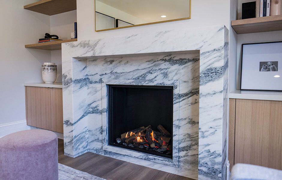 A fireplace with white marble surround, black hearth, built-in shelves, and a mirror