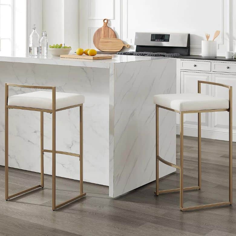 Modern kitchen with a white marble island and two gold-framed bar stools with white cushions